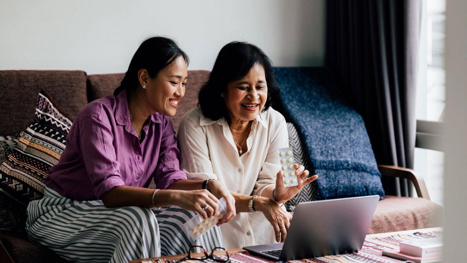 Two women huddled on a couch discussion medication on a virtual call